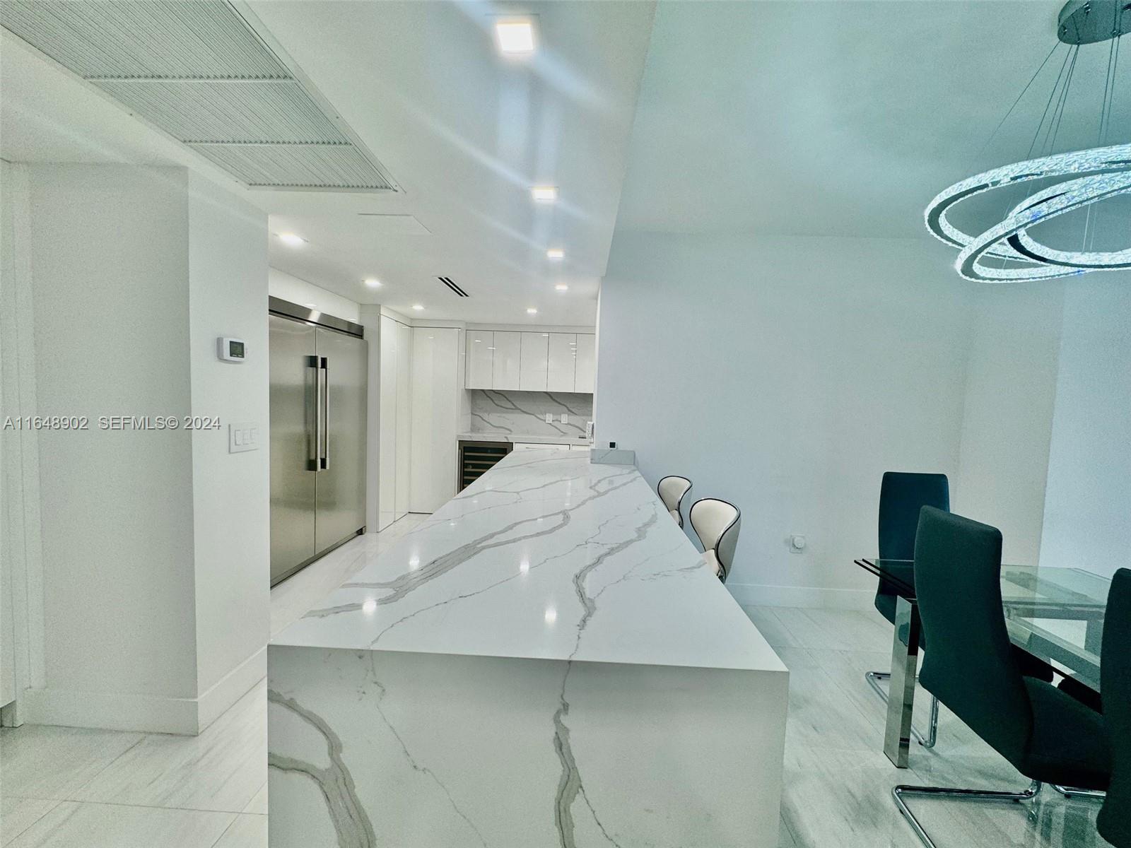 A modern kitchen features a large white marble waterfall island and stainless steel appliances — 9801 Collins Ave # 5U, Bal Harbour FL 33154, BAL HARBOUR, FL