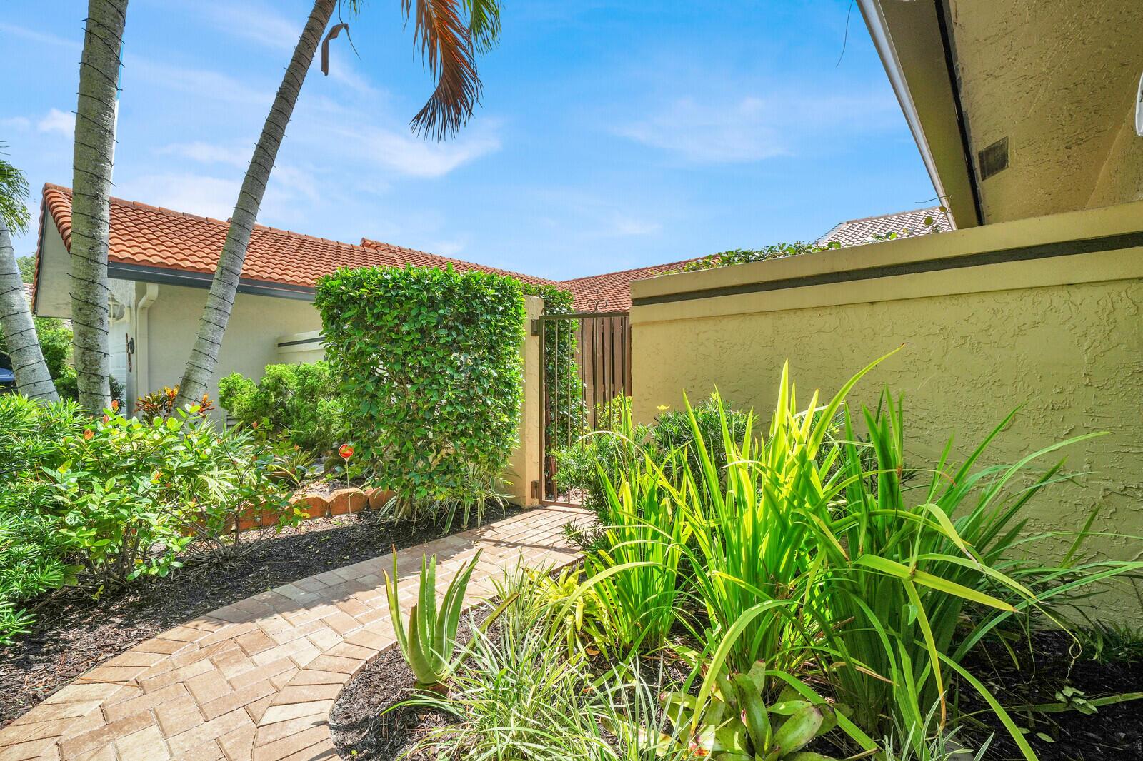 A brick walkway leads to a gated entrance beside a house with a tiled roof — 1735 NW 21st Court, Delray Beach FL 33445, DELRAY BEACH, FL