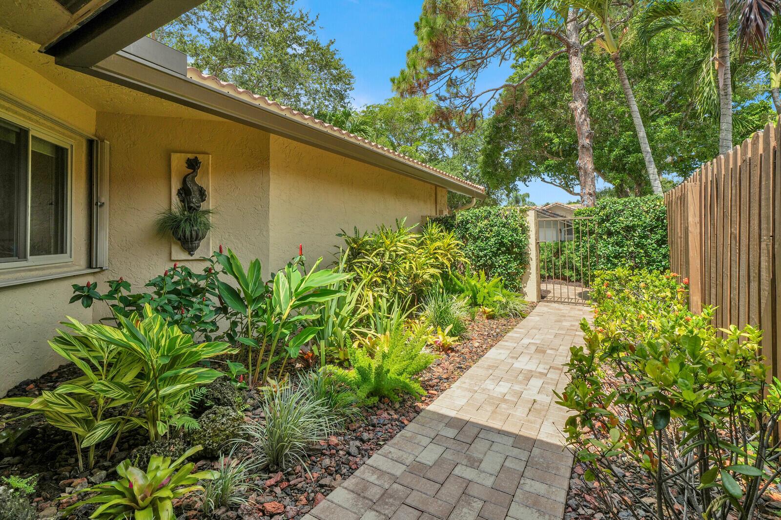 A paved walkway leads past a landscaped garden toward a metal gate beside a house — 1735 NW 21st Court, Delray Beach FL 33445, DELRAY BEACH, FL