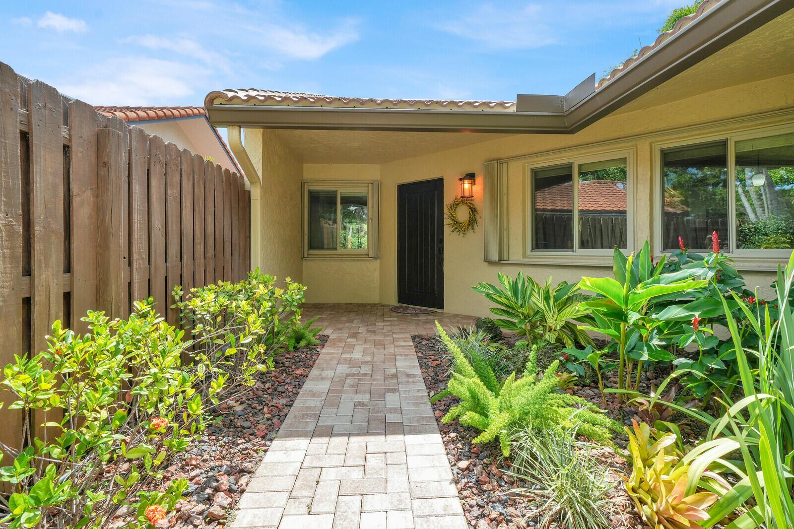 A paved walkway leads to the front entrance of a house with a wooden fence — 1735 NW 21st Court, Delray Beach FL 33445, DELRAY BEACH, FL