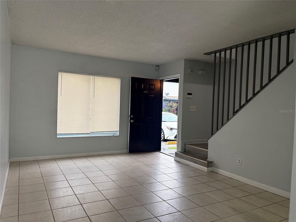 An interior view shows a tiled living room with a staircase and an open front door — 13045 LONDONDARY PLACE, TAMPA, FL