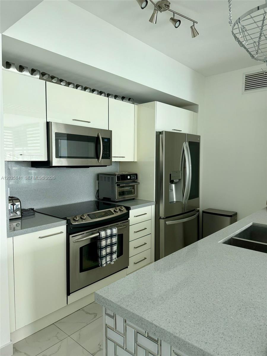 A modern kitchen features white cabinetry, stainless steel appliances, and a gray stone countertop — 951 Brickell Ave # 2810, Miami FL 33131, MIAMI, FL