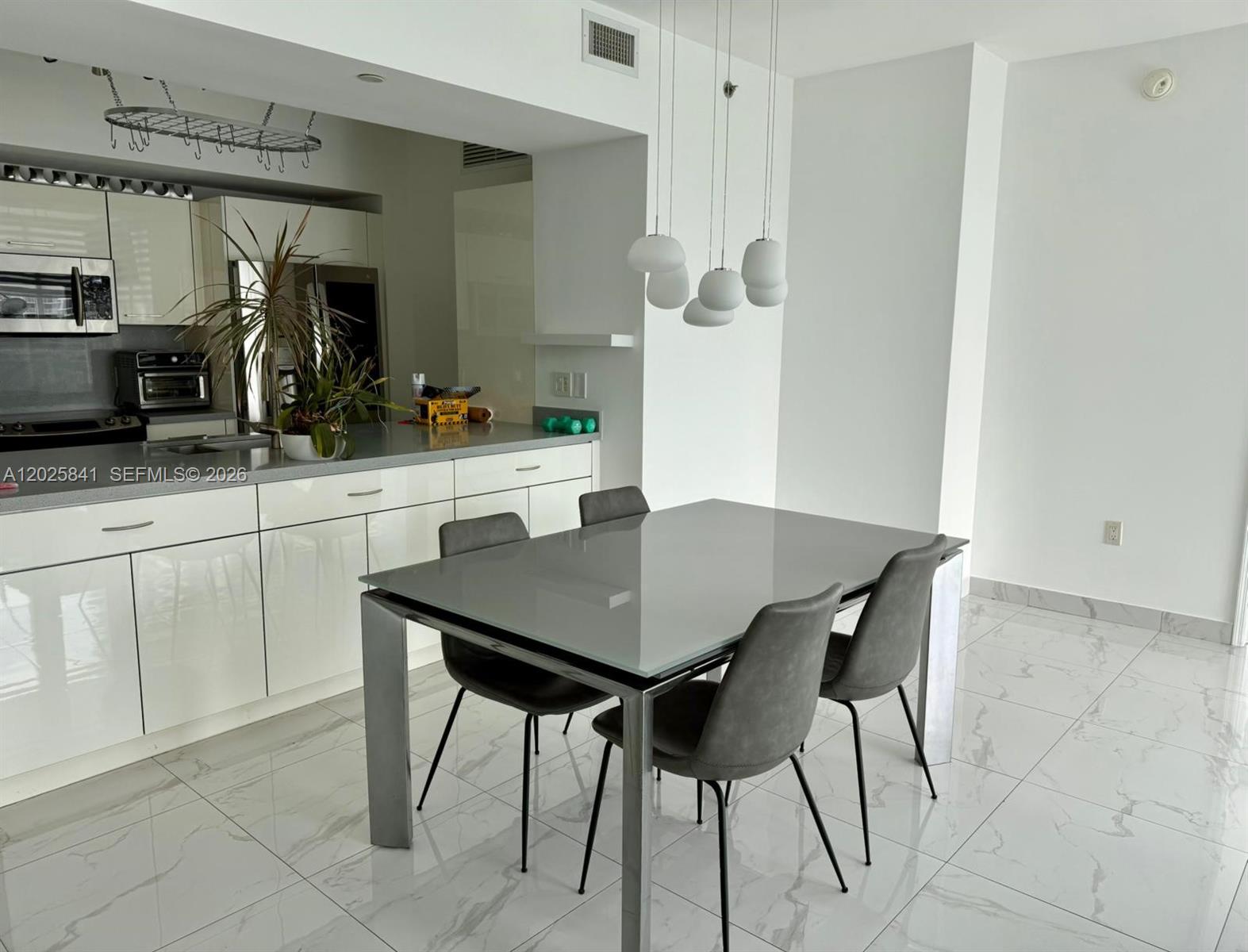 A modern kitchen with white cabinetry and a dining area featuring a glass-topped table — 951 Brickell Ave # 2810, Miami FL 33131, MIAMI, FL