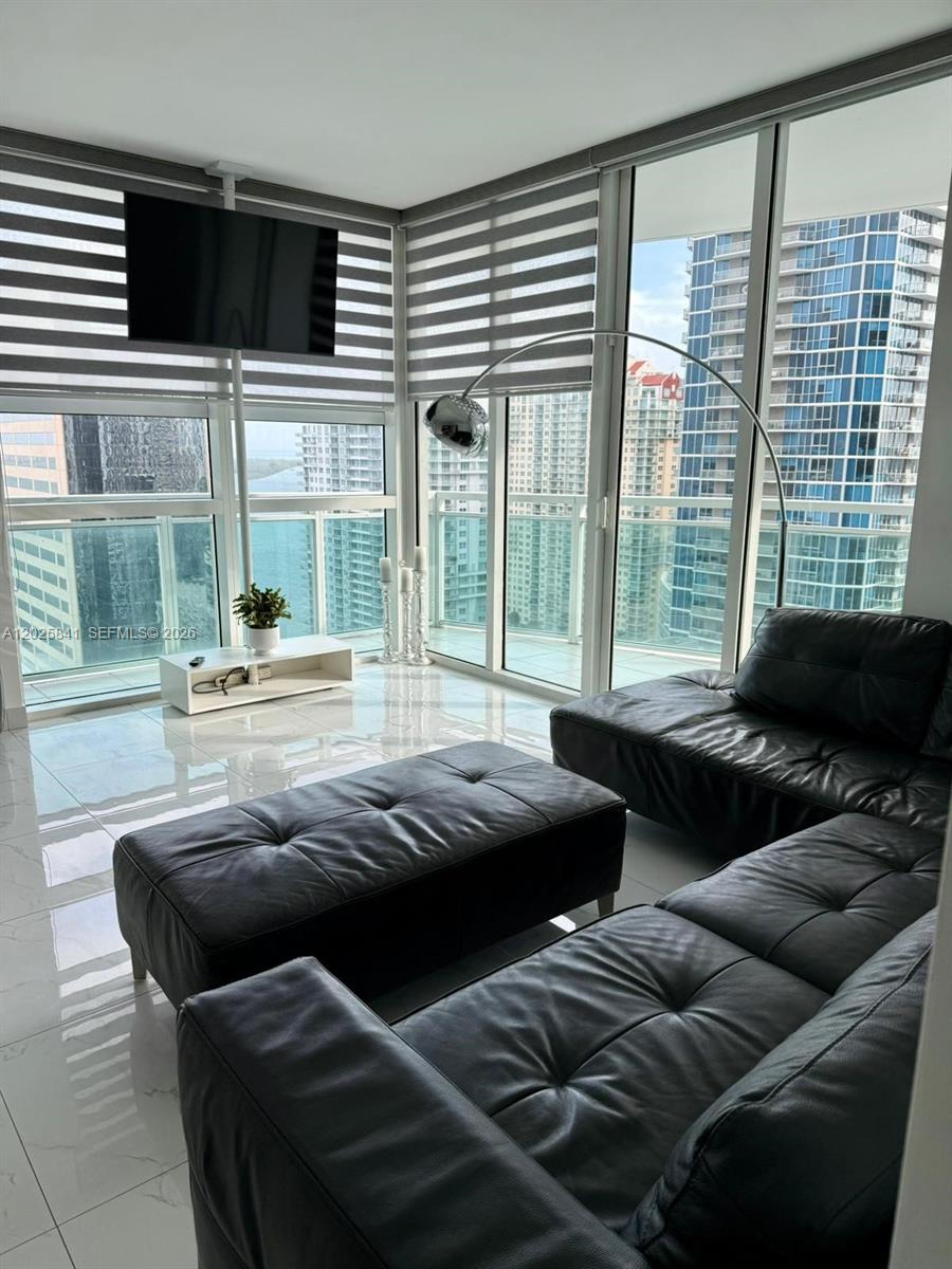 A modern living room features a black leather sectional, tiled floors, and floor-to-ceiling windows — 951 Brickell Ave # 2810, Miami FL 33131, MIAMI, FL