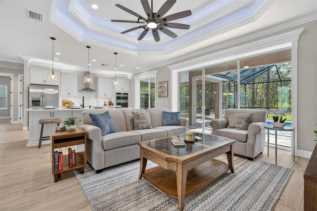 A living room with a tray ceiling, ceiling fan, and sliding doors opening to a pool — 5105 N PRINCEWOOD DRIVE, BEVERLY HILLS, FL
