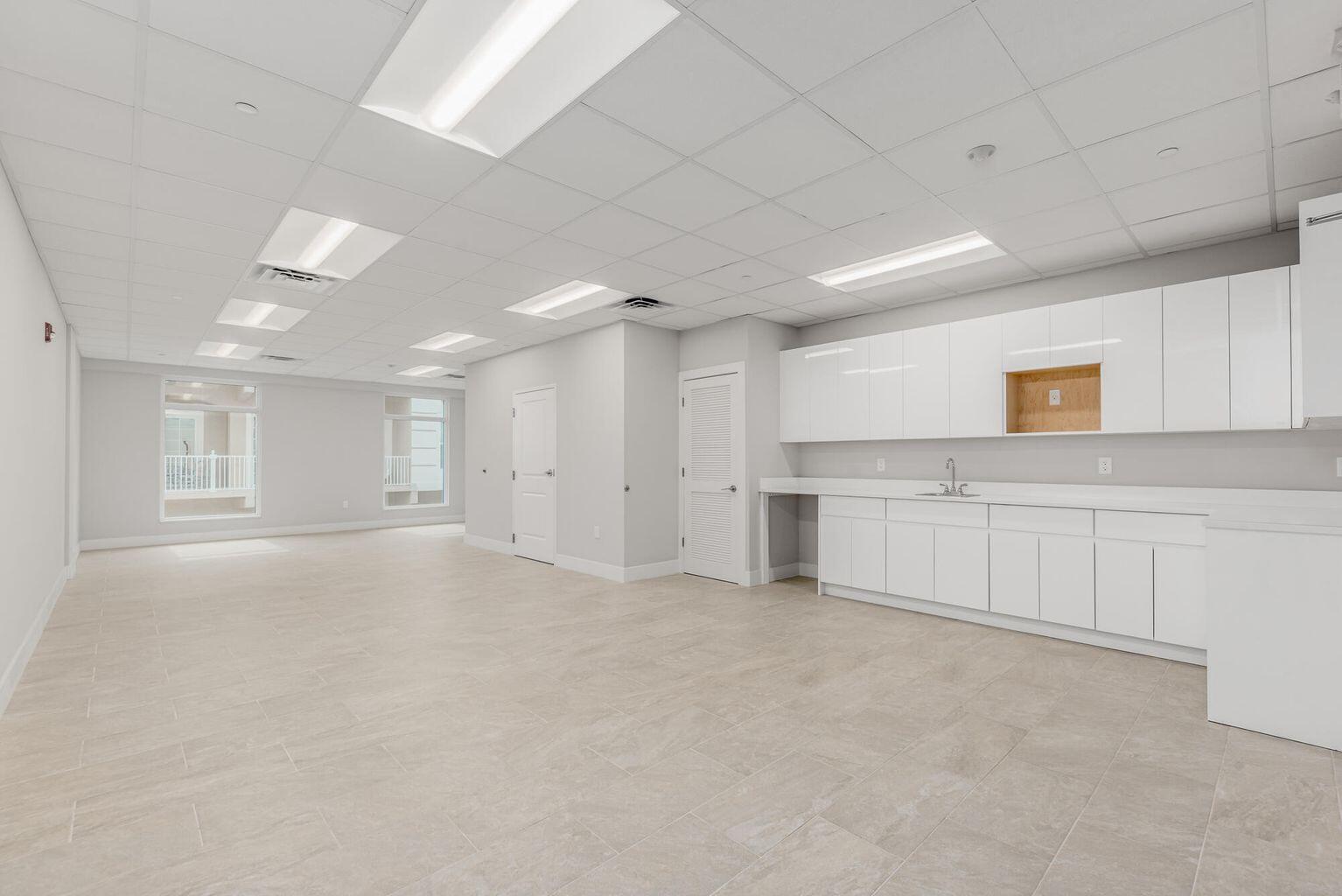 A bright, empty office space with white cabinetry, a kitchenette, and light-colored tile flooring — 41 SW Seminole Street # 210, Stuart FL 34994, STUART, FL