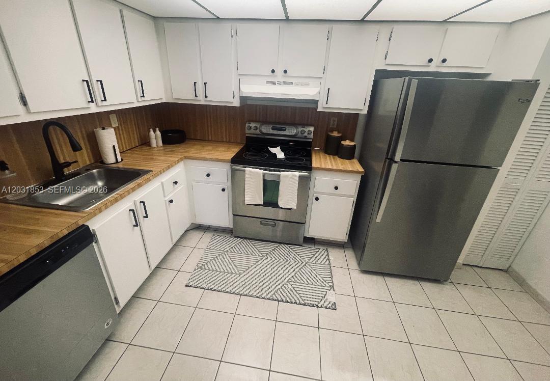 A kitchen features white cabinets, stainless steel appliances, a wood countertop, and tile flooring — 2625 Collins Ave # 502, Miami Beach FL 33140, MIAMI BEACH, FL