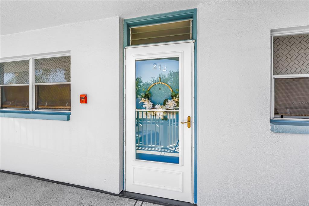 A white exterior door labeled 212 with a decorative wreath sits between two windows — 1868 SHORE DRIVE S UNIT 212, SOUTH PASADENA, FL