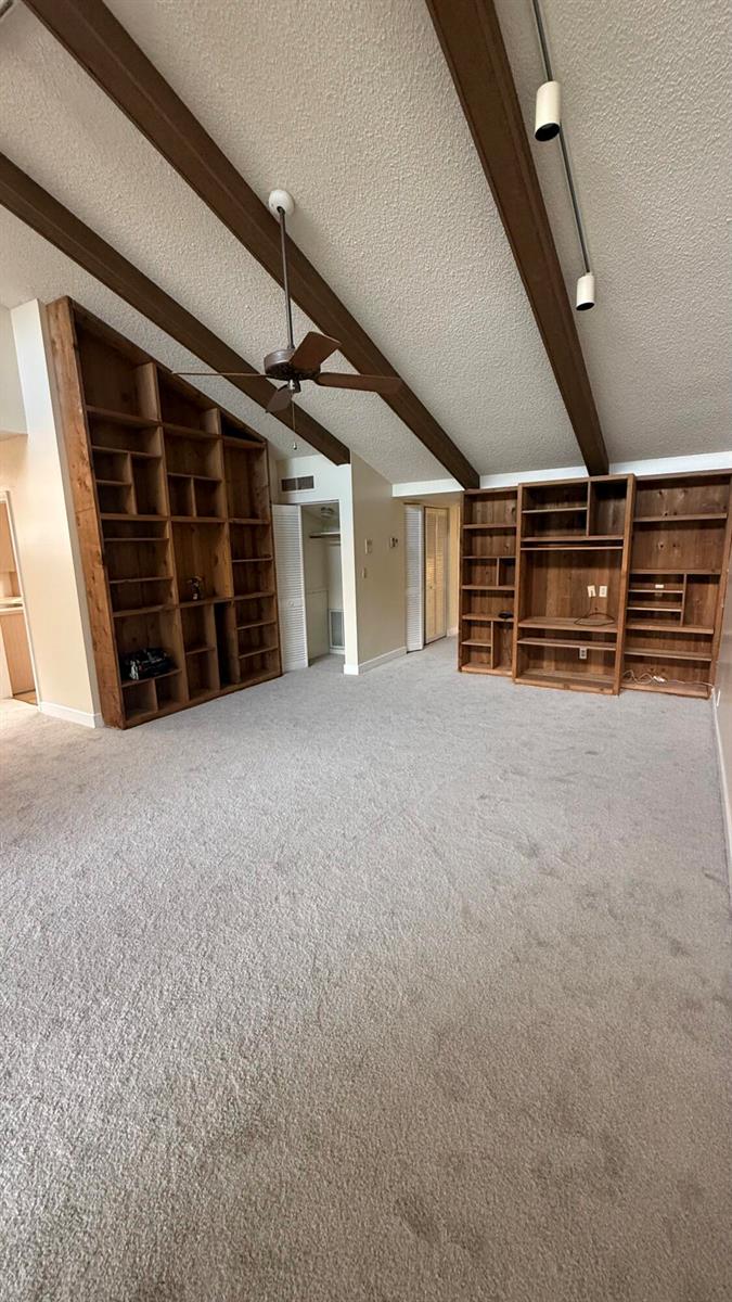 A living room with vaulted ceilings, exposed wooden beams, built-in shelving, and carpeted flooring — 6464 Pumpkin Seed Circle, Boca Raton FL 33433, BOCA RATON, FL