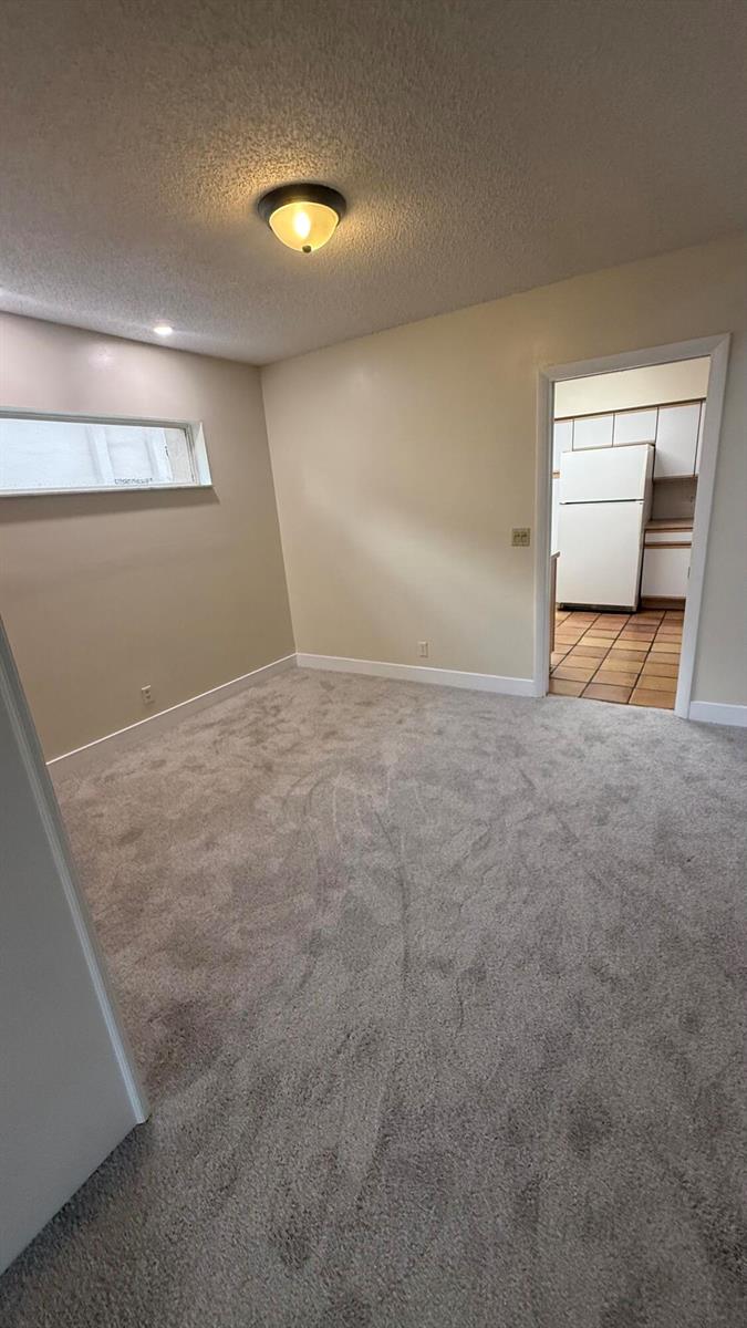 A carpeted room with a ceiling light and a doorway leading to a tiled kitchen — 6464 Pumpkin Seed Circle, Boca Raton FL 33433, BOCA RATON, FL
