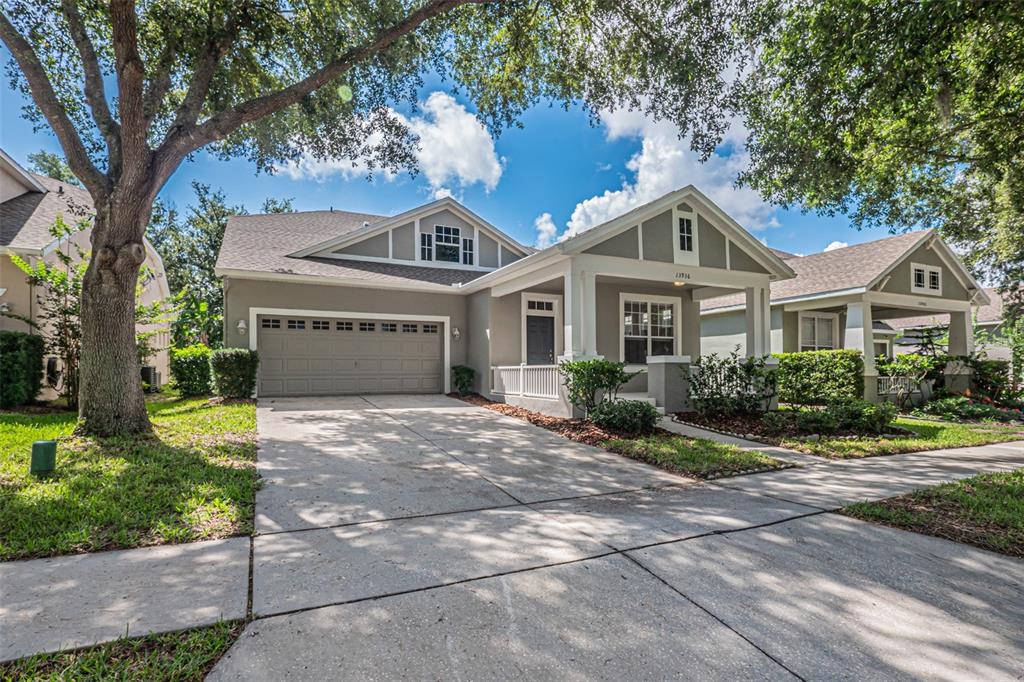 A gray single-story house with a two-car garage, front porch, and a large oak tree — 13936 EDEN ISLE BOULEVARD, WINDERMERE, FL