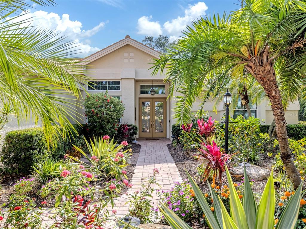 A paved walkway leads to the front entrance of a house surrounded by tropical landscaping — 417 WELLINGTON COURT, VENICE, FL