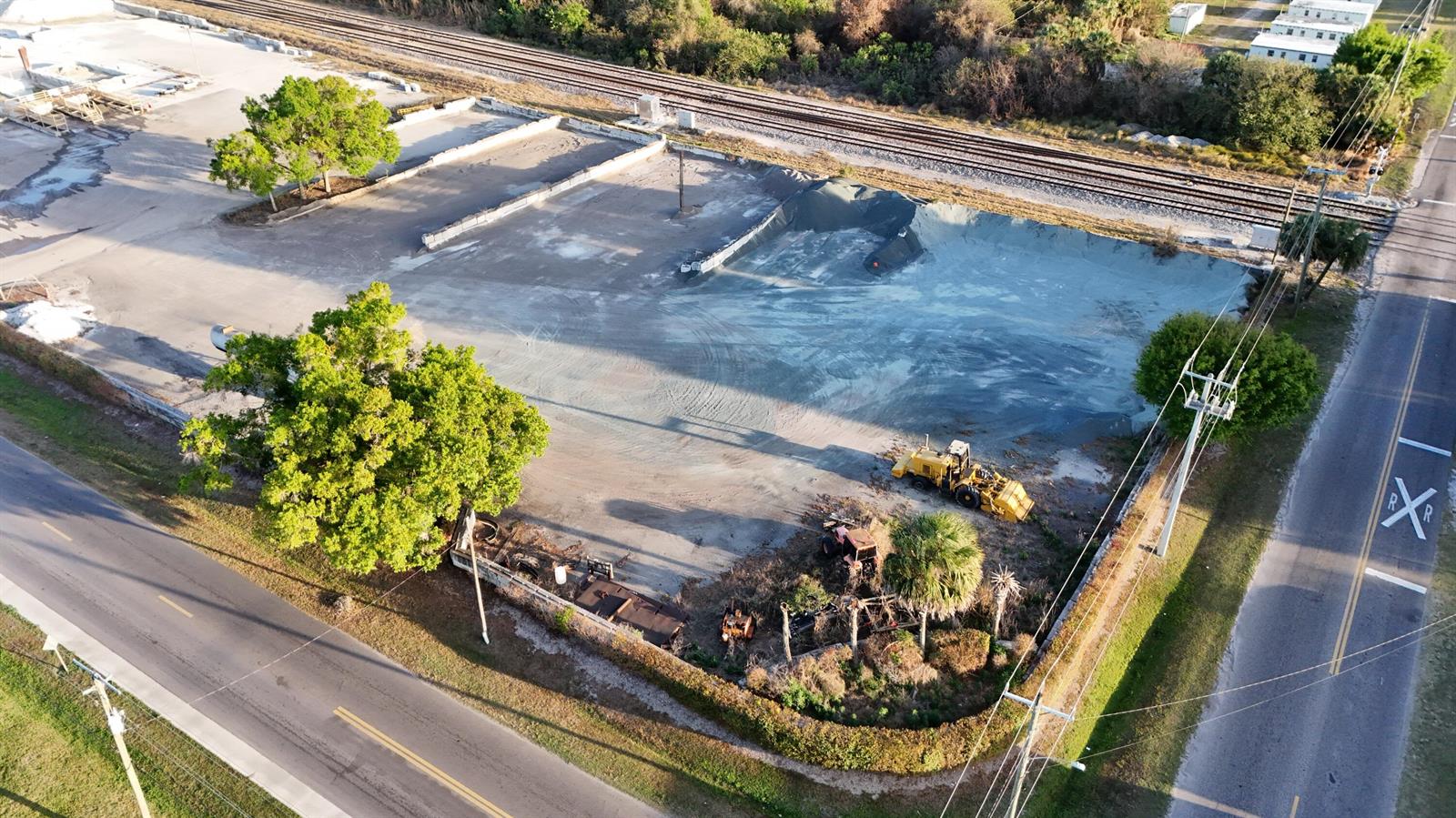 An aerial view shows a large, cleared industrial lot with a pile of gravel and machinery — 805 NW 9th Street, Okeechobee FL 34972, OKEECHOBEE, FL