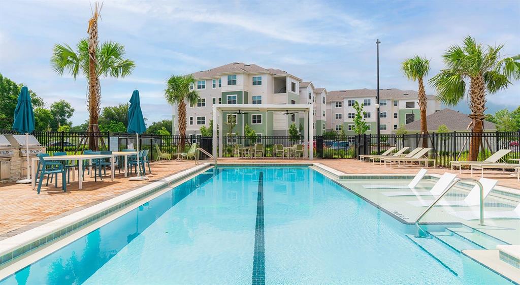 A swimming pool with a tanning ledge sits in front of a multi-story apartment building — 110 ZORA PLACE UNIT B1, ORLANDO, FL