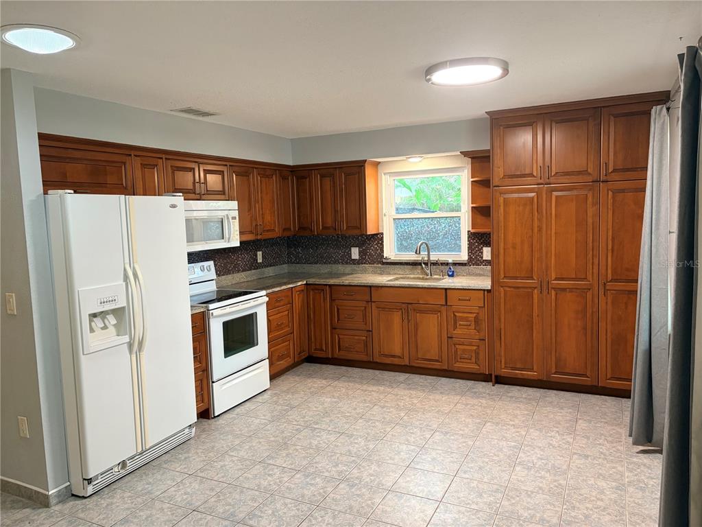 A kitchen features wood cabinets, white appliances, a tiled floor, and a window above the sink — 6010 TENNESSEE AVENUE, NEW PORT RICHEY, FL