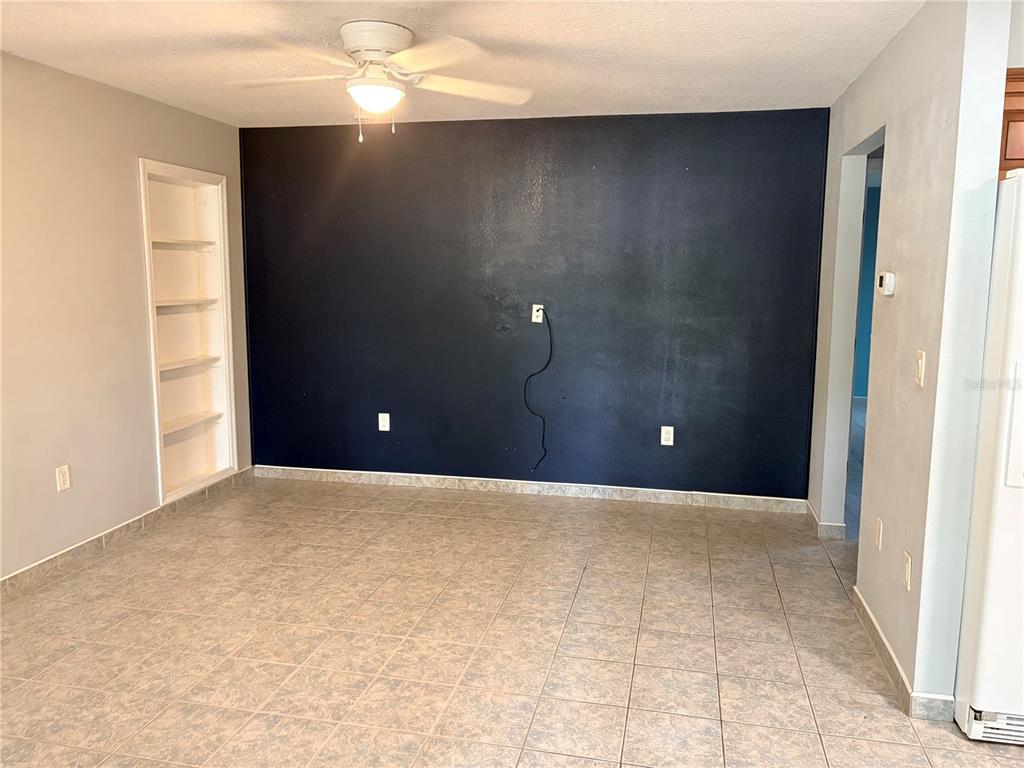 A room with tiled floors, a dark accent wall, a ceiling fan, and built-in shelving — 6010 TENNESSEE AVENUE, NEW PORT RICHEY, FL