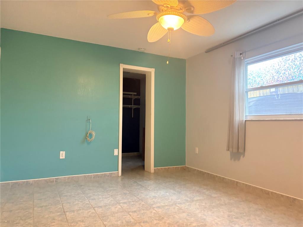 A bedroom with light blue walls, tile flooring, a ceiling fan, and a walk-in closet — 6010 TENNESSEE AVENUE, NEW PORT RICHEY, FL