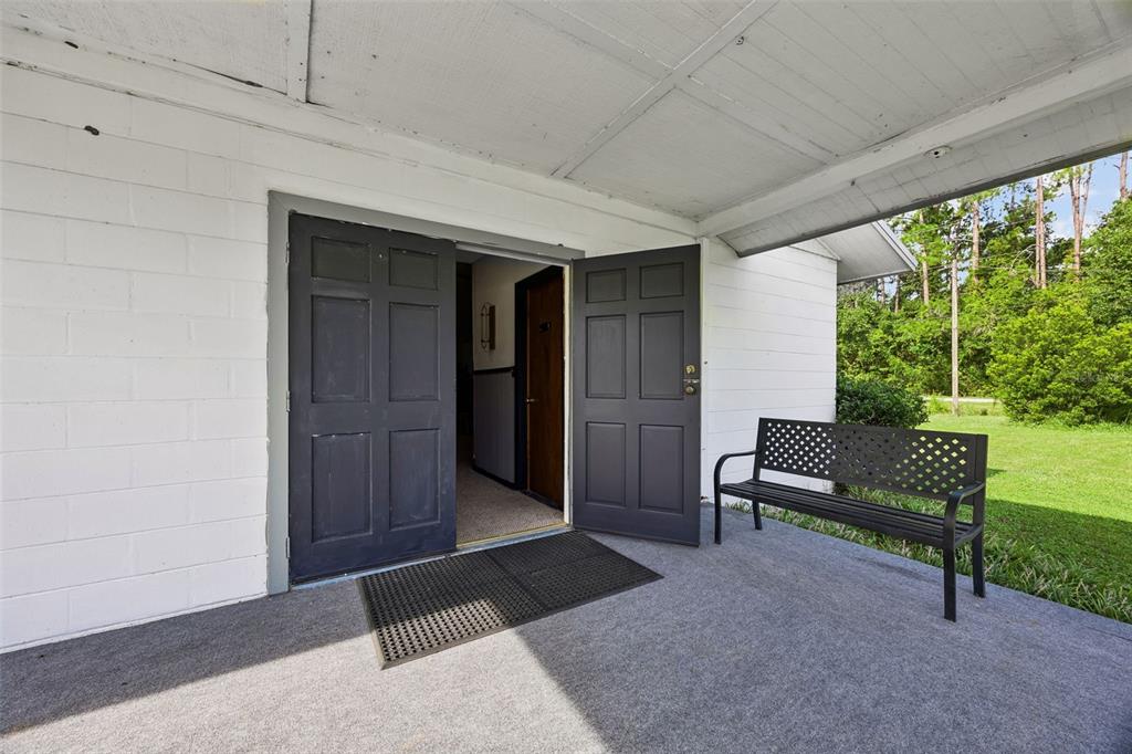 A covered concrete porch features a black bench and double doors opening into a building — 101 SESAME STREET, PALATKA, FL