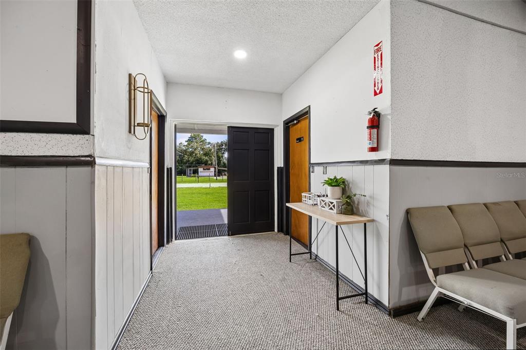 An interior hallway features gray wainscoting, carpeted flooring, a console table, and an open exterior door — 101 SESAME STREET, PALATKA, FL