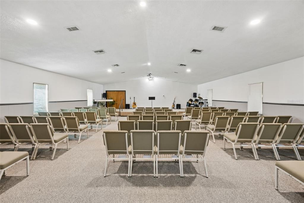 A large, carpeted room set up with rows of chairs facing a small stage — 101 SESAME STREET, PALATKA, FL