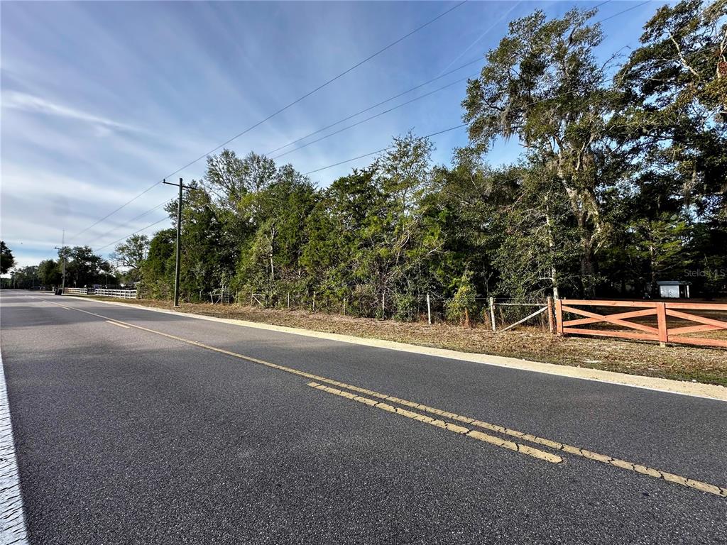 A paved road runs alongside a wooded lot enclosed by a wooden fence — NE 60TH AVENUE, HIGH SPRINGS, FL
