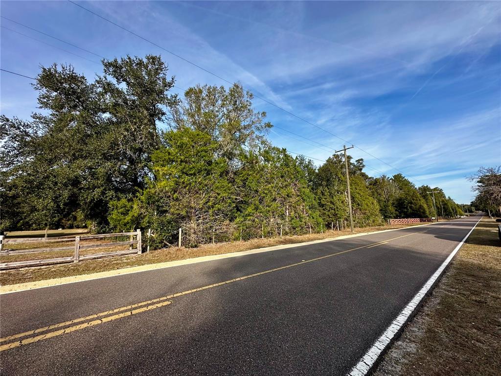 A paved road runs alongside a wooded lot bordered by a wooden fence — NE 60TH AVENUE, HIGH SPRINGS, FL