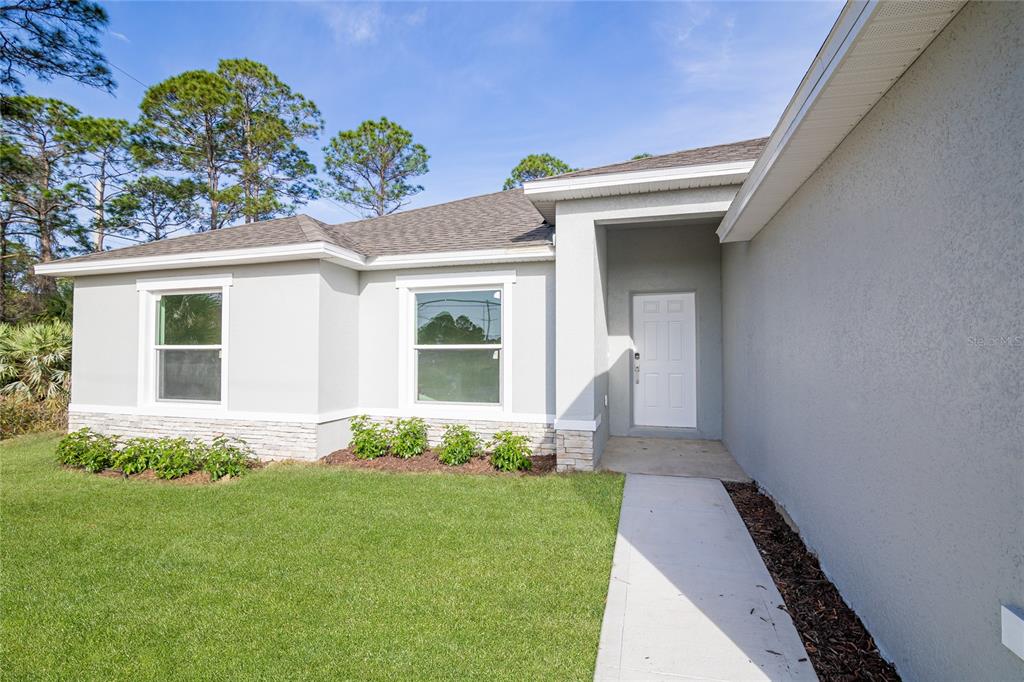 A light gray house exterior features a white front door, stone accents, and green landscaping — 1917 TRAPPER AVENUE SE, PALM BAY, FL