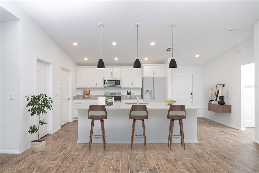 A modern kitchen features white cabinetry, a granite island with three stools, and wood-look flooring — 1917 TRAPPER AVENUE SE, PALM BAY, FL