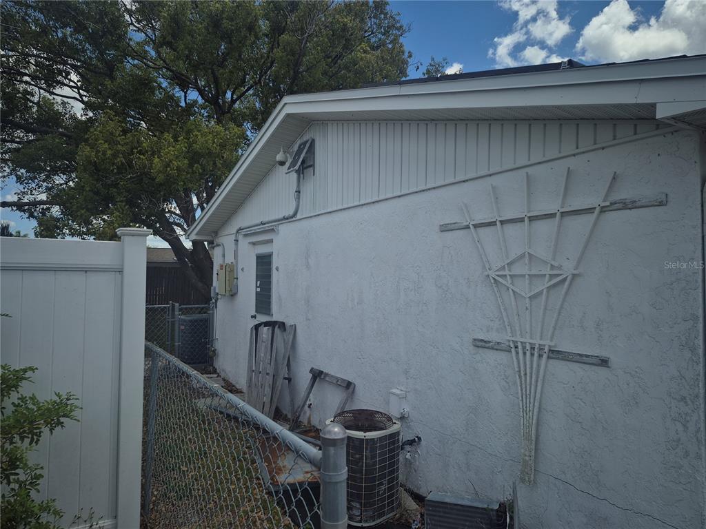 The exterior side of a white stucco house features an air conditioning unit and trellis — 3245 FAIRMOUNT DRIVE, HOLIDAY, FL