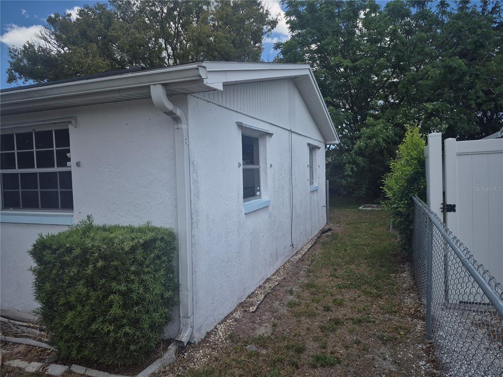 The exterior side of a white stucco house features a downspout and two windows — 3245 FAIRMOUNT DRIVE, HOLIDAY, FL