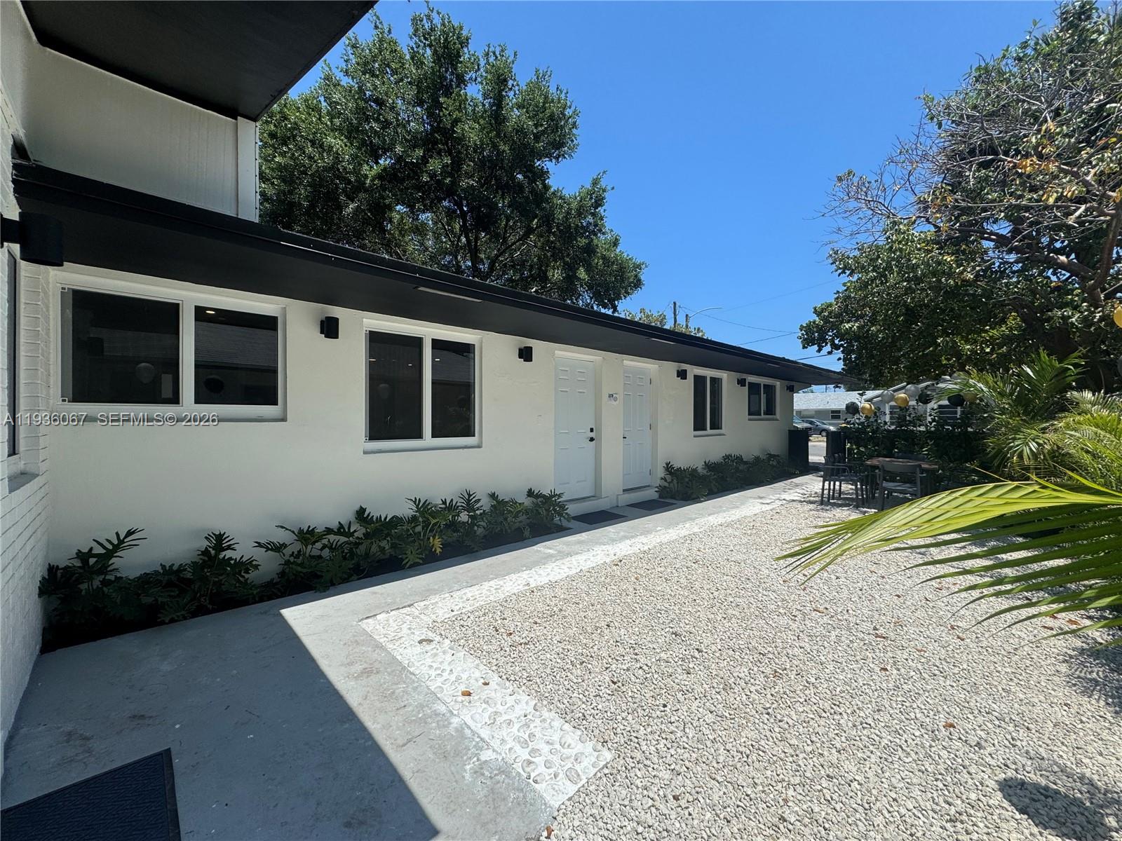 A white exterior building features two entry doors, windows, and a gravel courtyard area — 111 NW 7th Ave, Dania Beach FL 33004, DANIA BEACH, FL
