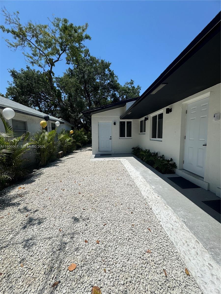 A gravel walkway leads between two white buildings with black trim under a clear sky — 111 NW 7th Ave, Dania Beach FL 33004, DANIA BEACH, FL