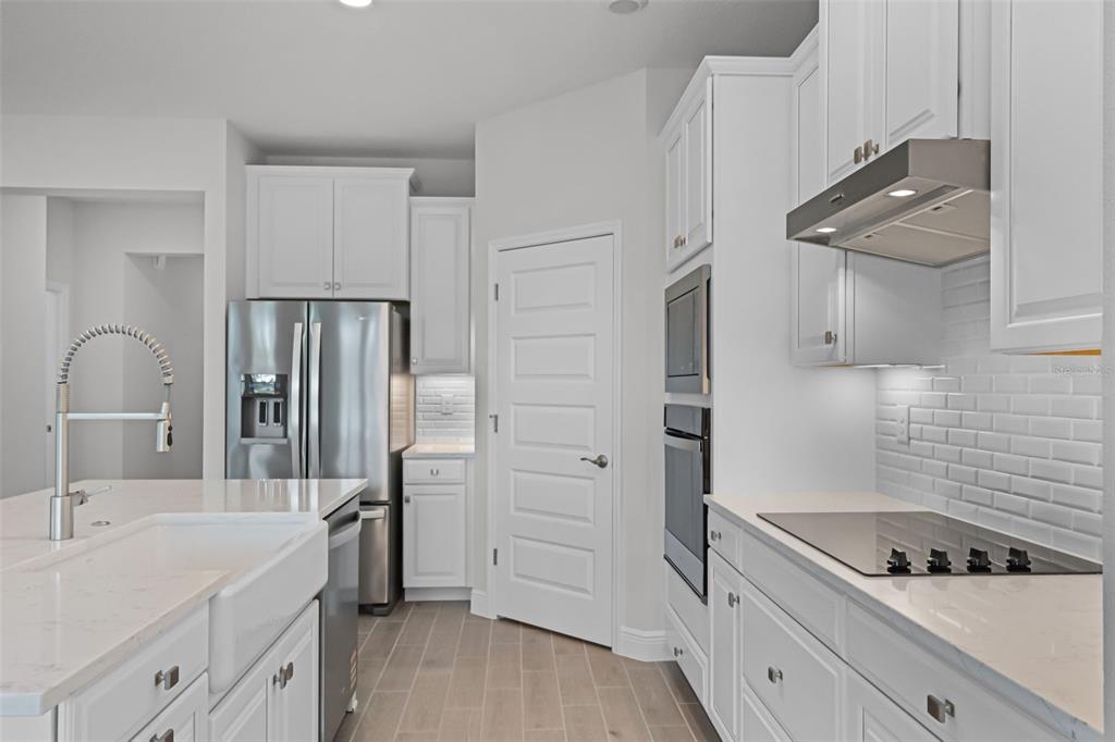 A modern kitchen features white cabinetry, stainless steel appliances, a farmhouse sink, and quartz countertops — 11899 SHINE VIEW LANE, WINTER GARDEN, FL