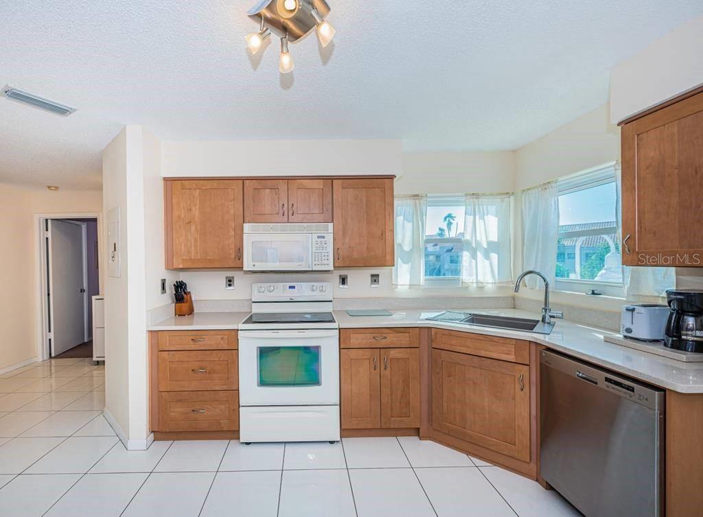 A kitchen with wood cabinets, white appliances, a corner sink, and white tile flooring — 6151 BAHIA DEL MAR BOULEVARD UNIT 226, ST PETERSBURG, FL