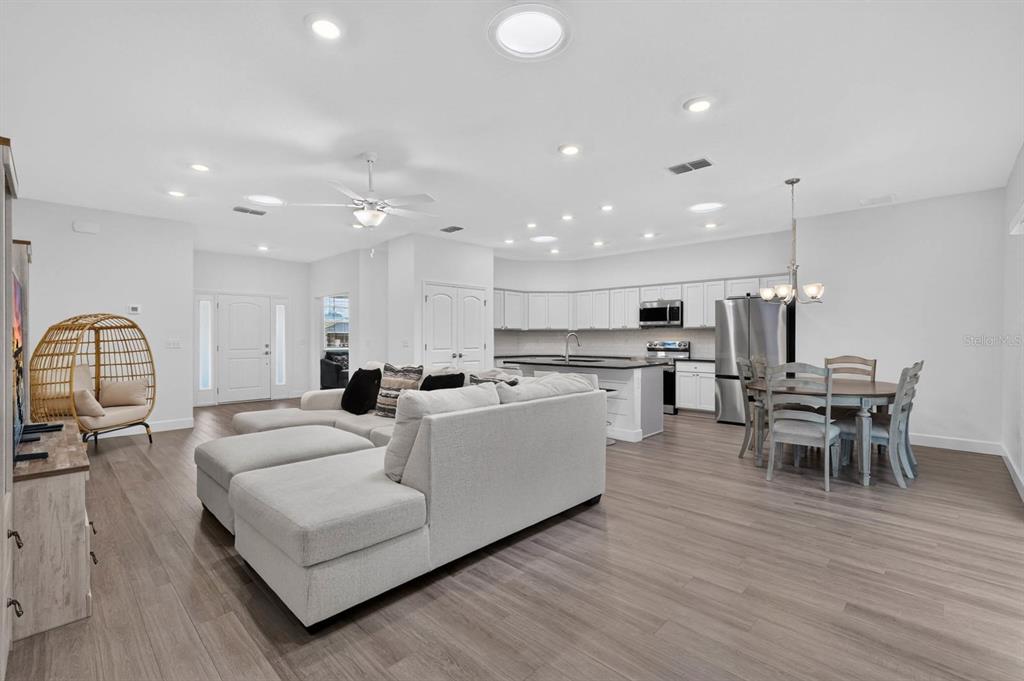 An open-concept living room and kitchen with light wood floors, white cabinetry, and a sectional — 23 BUD FIELD DRIVE, PALM COAST, FL