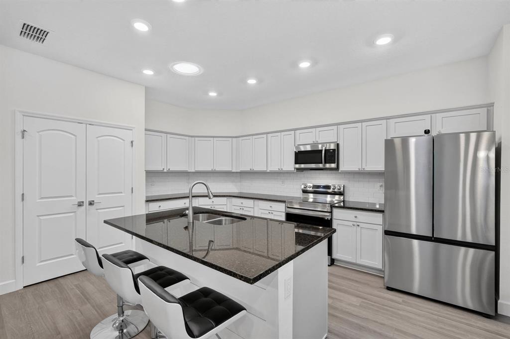 A modern kitchen features white cabinets, dark granite countertops, stainless steel appliances, and a breakfast island — 23 BUD FIELD DRIVE, PALM COAST, FL