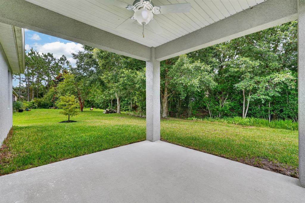 A covered concrete patio overlooks a grassy backyard with trees and a ceiling fan — 23 BUD FIELD DRIVE, PALM COAST, FL