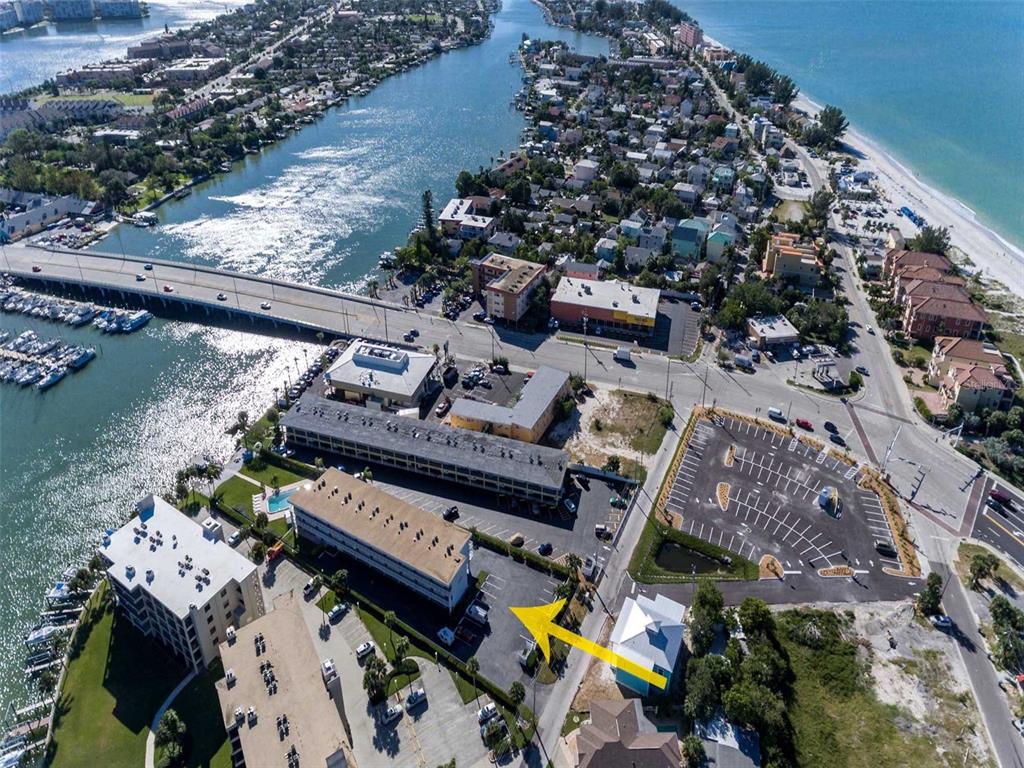 An aerial view shows a coastal hotel property with a parking lot and bridge — 9755 HARRELL AVENUE UNIT 102, TREASURE ISLAND, FL