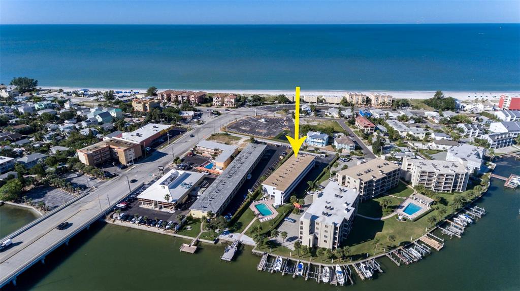 An aerial view shows a multi-story apartment complex near a beach and a bridge — 9755 HARRELL AVENUE UNIT 102, TREASURE ISLAND, FL