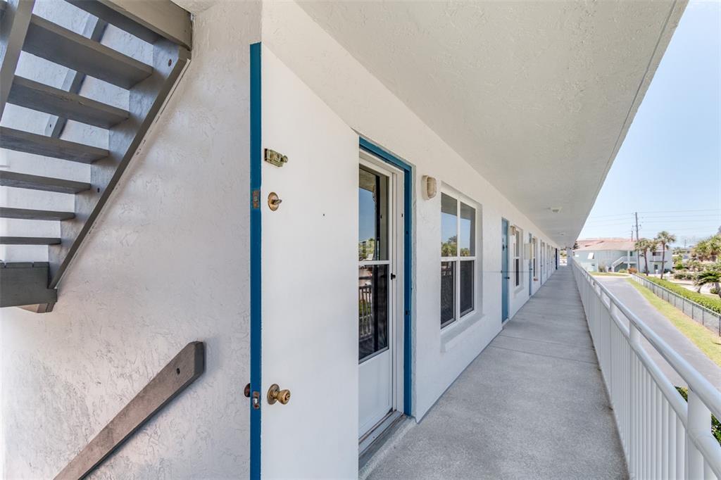 An exterior walkway with a white wall, a door, and a metal railing — 9755 HARRELL AVENUE UNIT 102, TREASURE ISLAND, FL