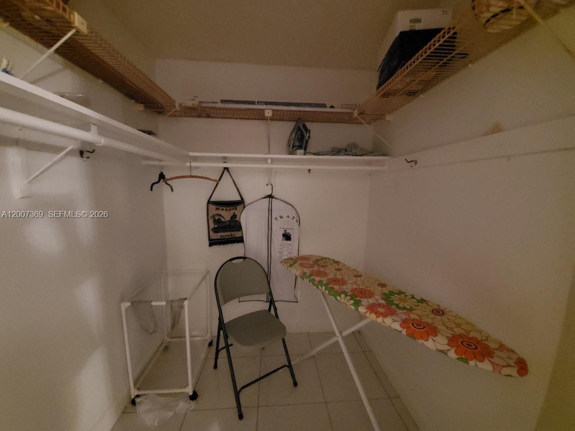 A walk-in closet contains a folding chair, an ironing board, and wire shelving — 1750 NE 191st St # 1, Miami FL 33179, MIAMI, FL