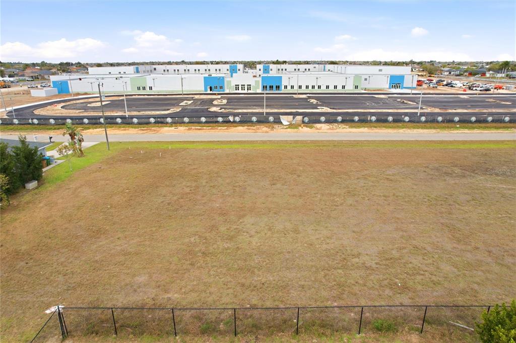 An aerial view shows a vacant, fenced-in grassy lot across from a large commercial building — 217 NW 20TH AVENUE, CAPE CORAL, FL