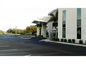 A modern white office building features a prominent angled entrance canopy and a paved parking lot — 3180 CURLEW ROAD UNIT 107, OLDSMAR, FL
