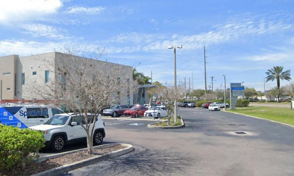 A parking lot sits in front of a commercial building under a blue sky — 3180 CURLEW ROAD UNIT 107, OLDSMAR, FL