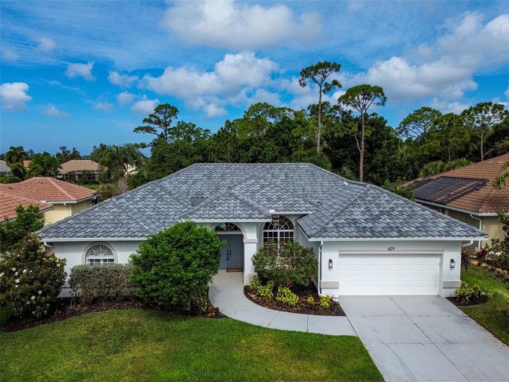 A single-story house with a gray tile roof, white stucco walls, and a two-car garage — 629 SAWGRASS BRIDGE ROAD, VENICE, FL