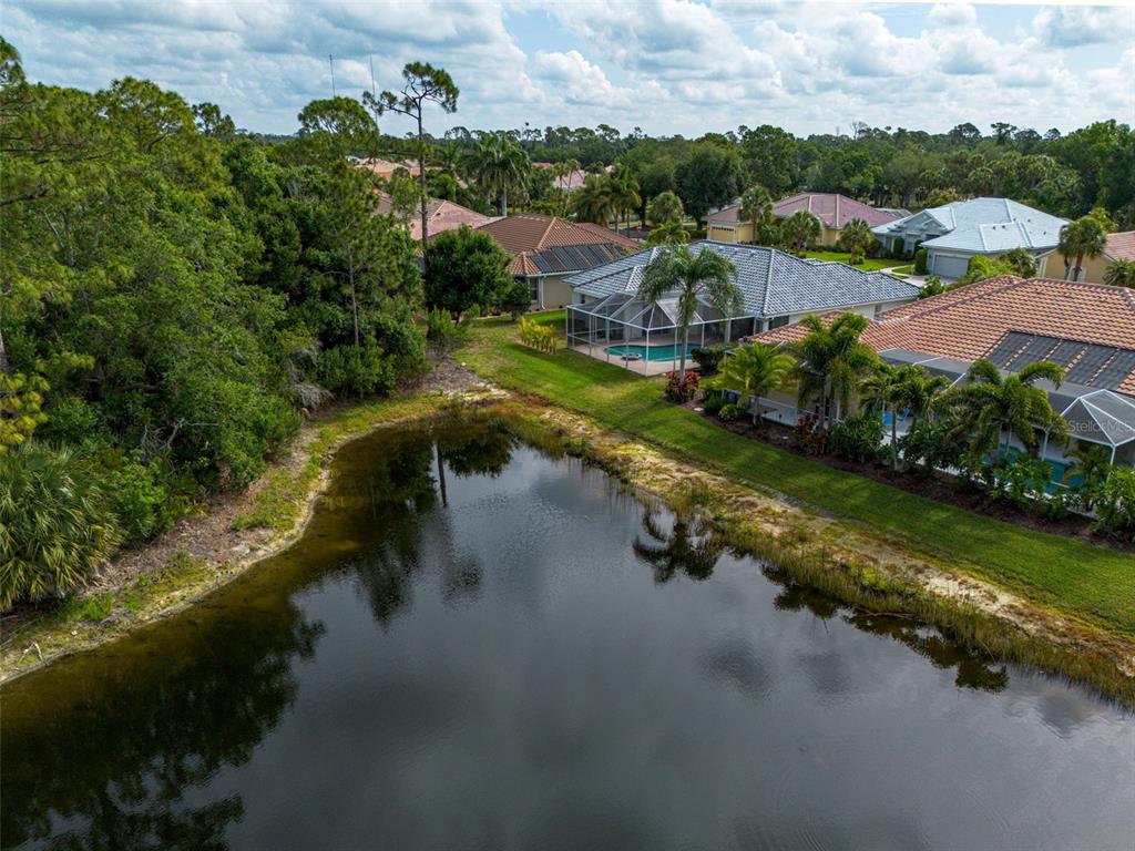 An aerial view shows a pond in the foreground with several houses and palm trees behind — 629 SAWGRASS BRIDGE ROAD, VENICE, FL