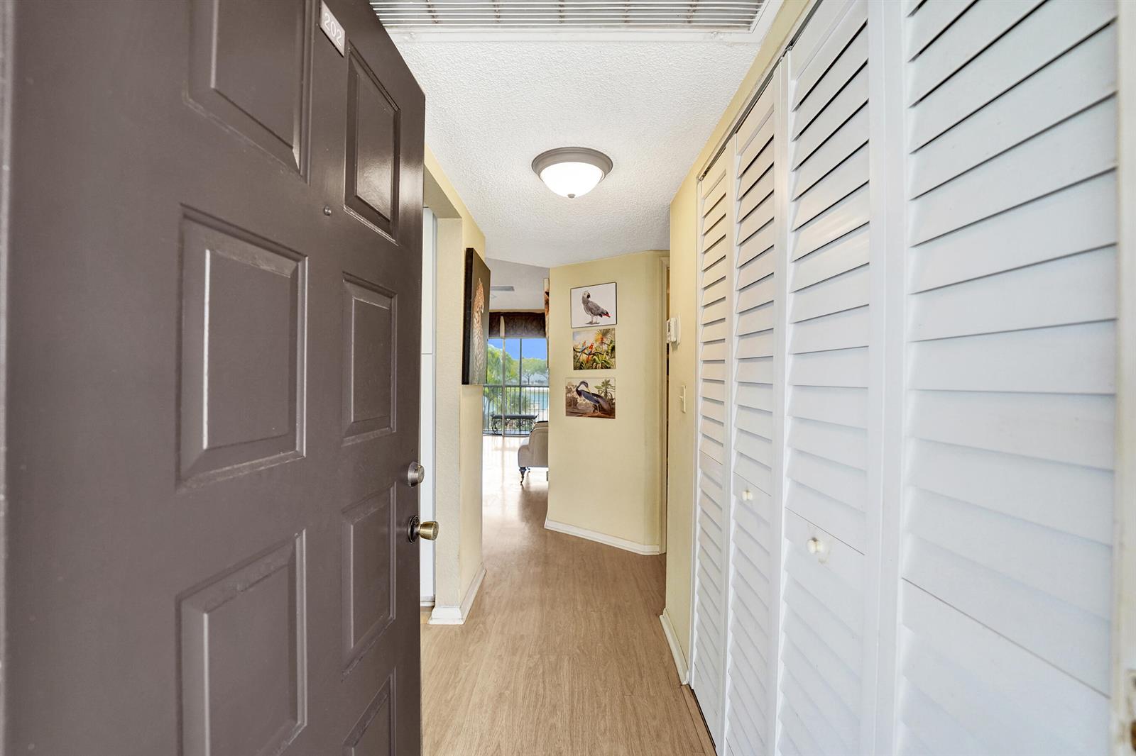 An entryway features a brown door, light wood flooring, louvered closet doors, and wall art — 5531 Lakeside Drive # 202, Margate FL 33063, MARGATE, FL