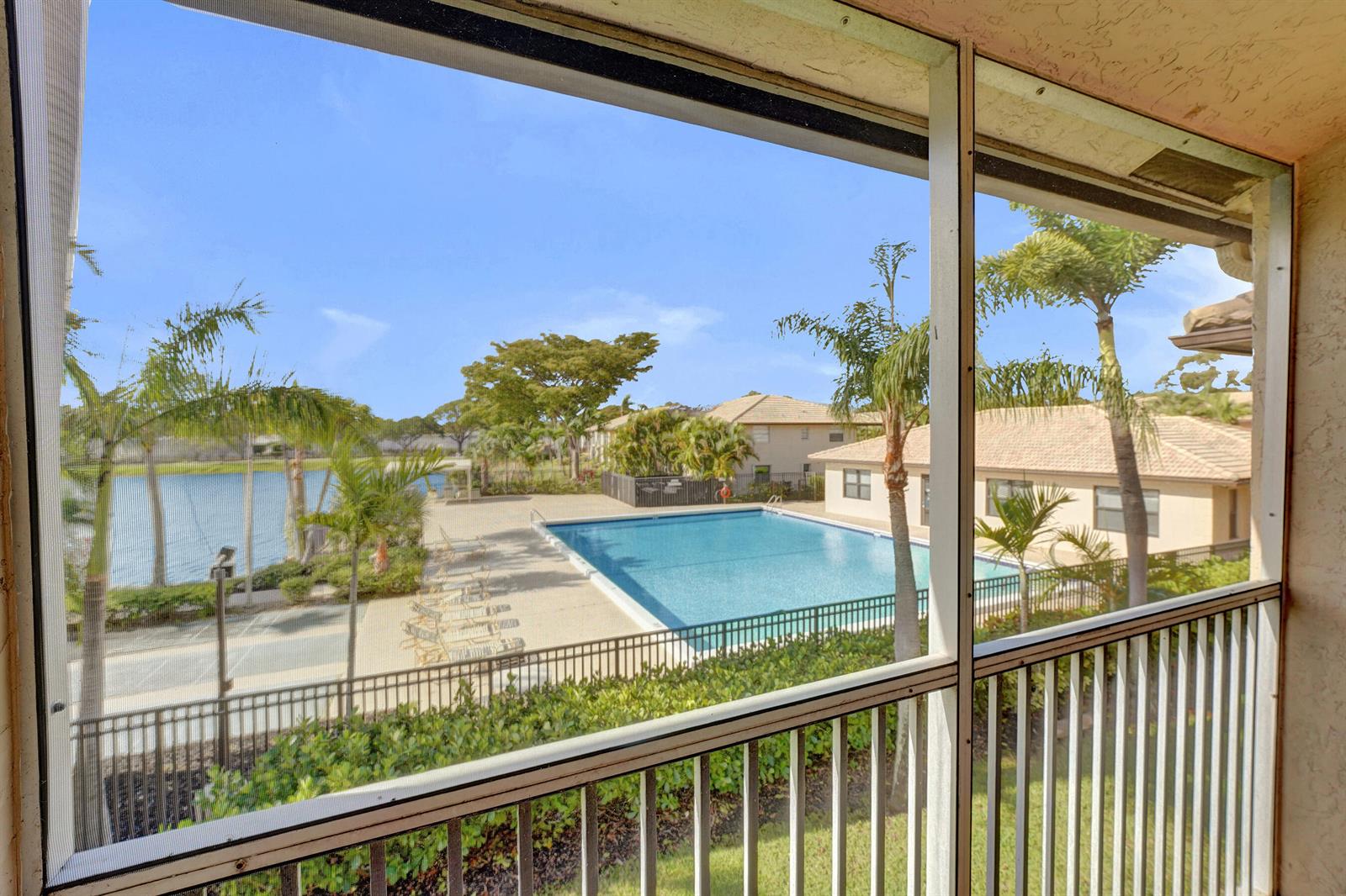 A view from a screened balcony overlooking a swimming pool, lake, and residential buildings — 5531 Lakeside Drive # 202, Margate FL 33063, MARGATE, FL