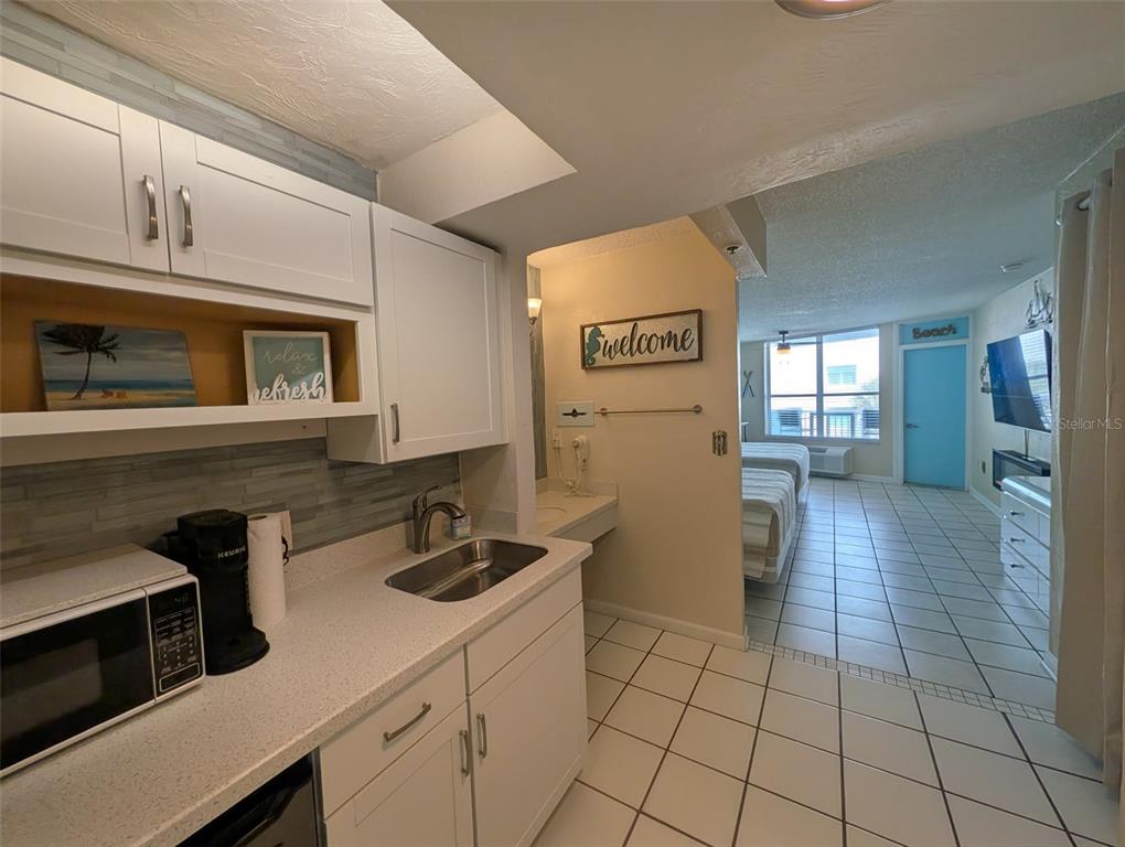 A kitchenette with white cabinets and a sink opens into a bedroom with tile floors — 313 S ATLANTIC AVENUE UNIT 3100, DAYTONA BEACH, FL