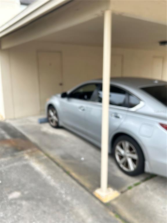 A silver sedan is parked in a covered carport next to a closed door — 2462 KINGFISHER LANE UNIT J203, CLEARWATER, FL